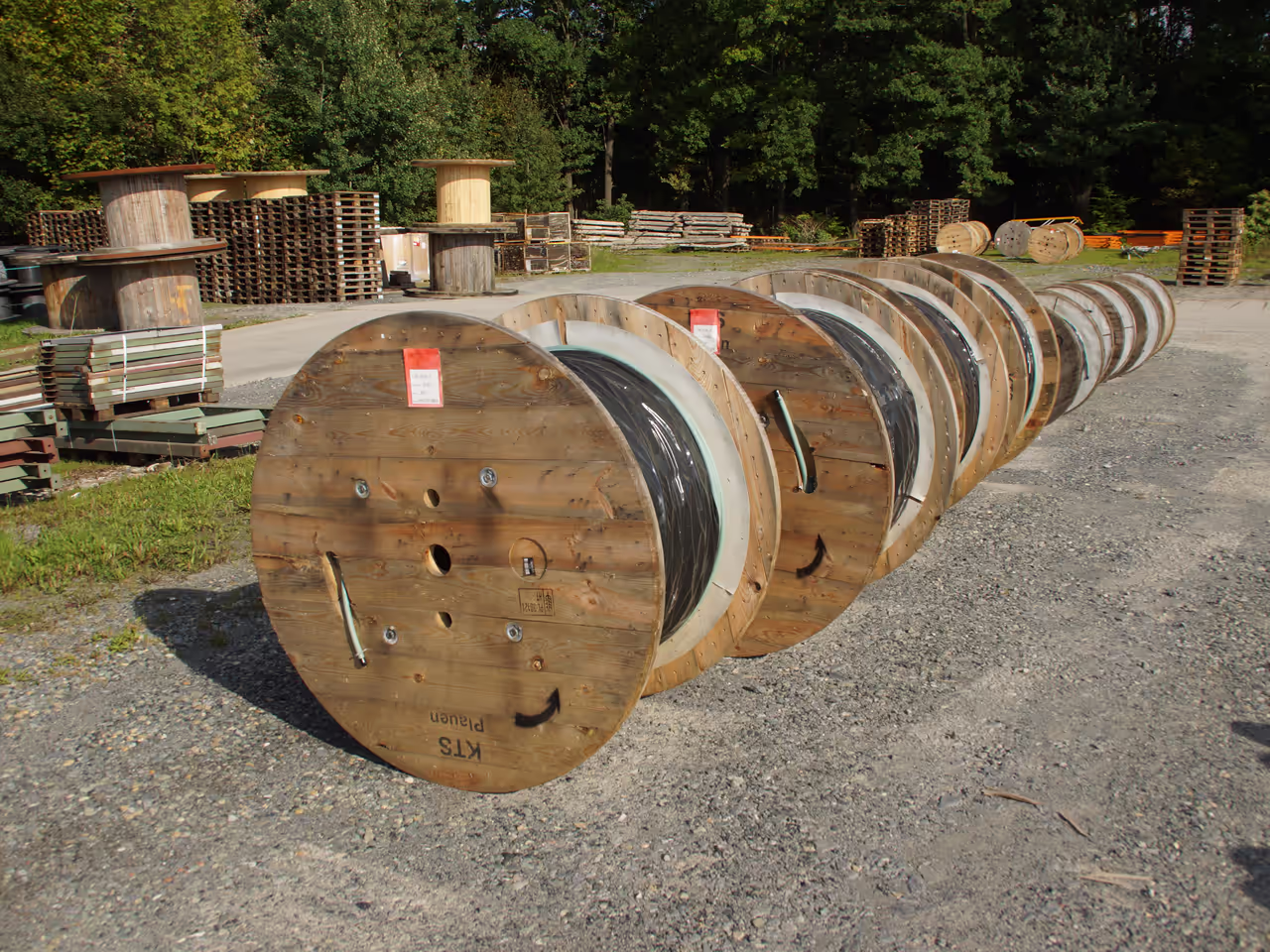 Row of reusable KTS wooden cable drums with wound industrial cable in a drum yard